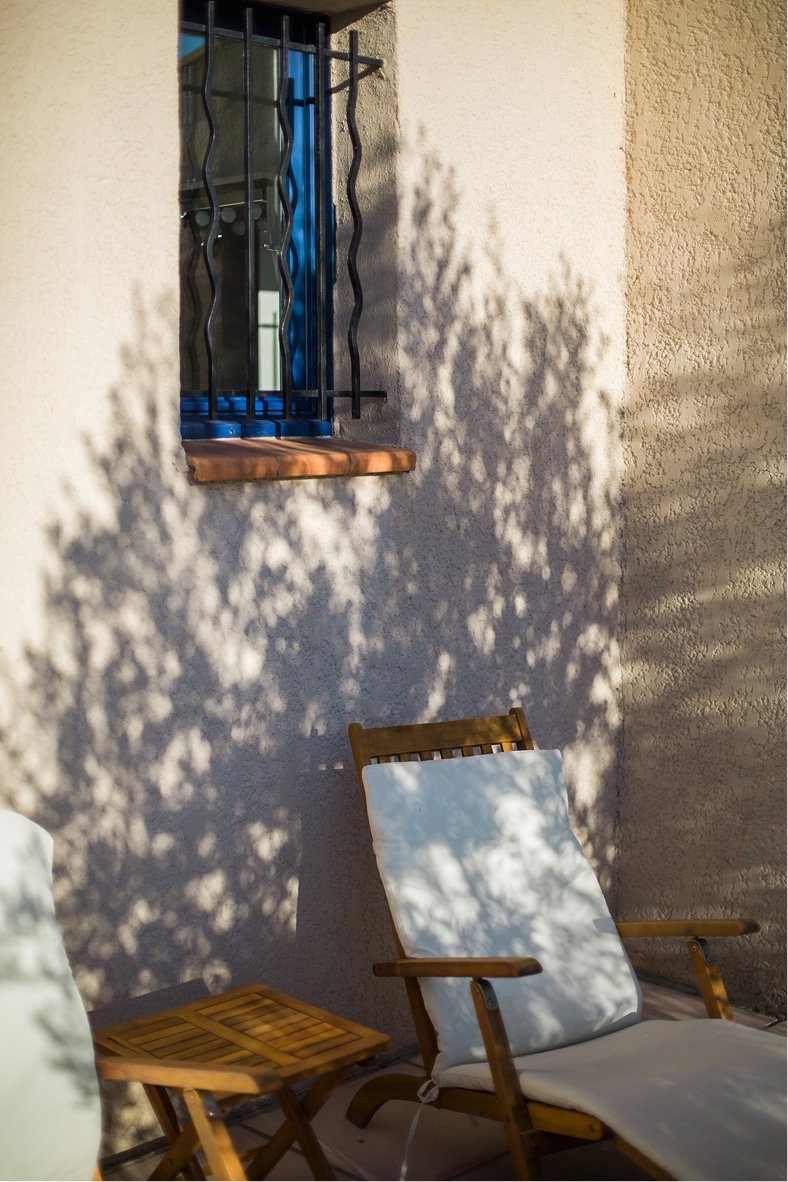 Ombres d'olivier sur le mur, près des chaises longues et de la fenêtre aux volets bleus